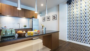 Une cuisine moderne avec des meubles en bois, un réfrigérateur en acier inoxydable, un grille-pain vintage et un grand îlot central doté d’un plan de travail noir.