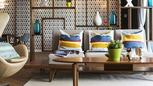 Un salon moderne avec un canapé, un fauteuil et une table basse. On y trouve des étagères décoratives ornées de plantes et de vases.