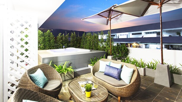 Une terrasse sur le toit, aménagée avec des meubles en osier, un jacuzzi et des plantes en pot.