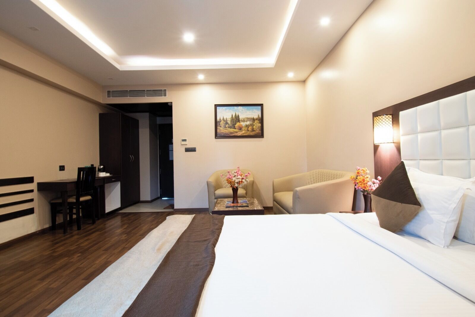 A hotel room with a bed, a desk, two chairs, a coffee table, and a painting on the wall.