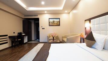 A hotel room with a bed, a desk, two chairs, a coffee table, and a painting on the wall.