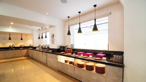 A modern kitchen with a long counter, overhead pendant lights, and a window with blinds. - Akshaya Aura (Bengaluru)