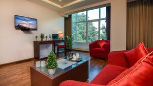 A modern living room with a red sofa, a glass coffee table, a flat-screen TV, and a large window with a view of trees. - Akshaya Aura (Bengaluru)
