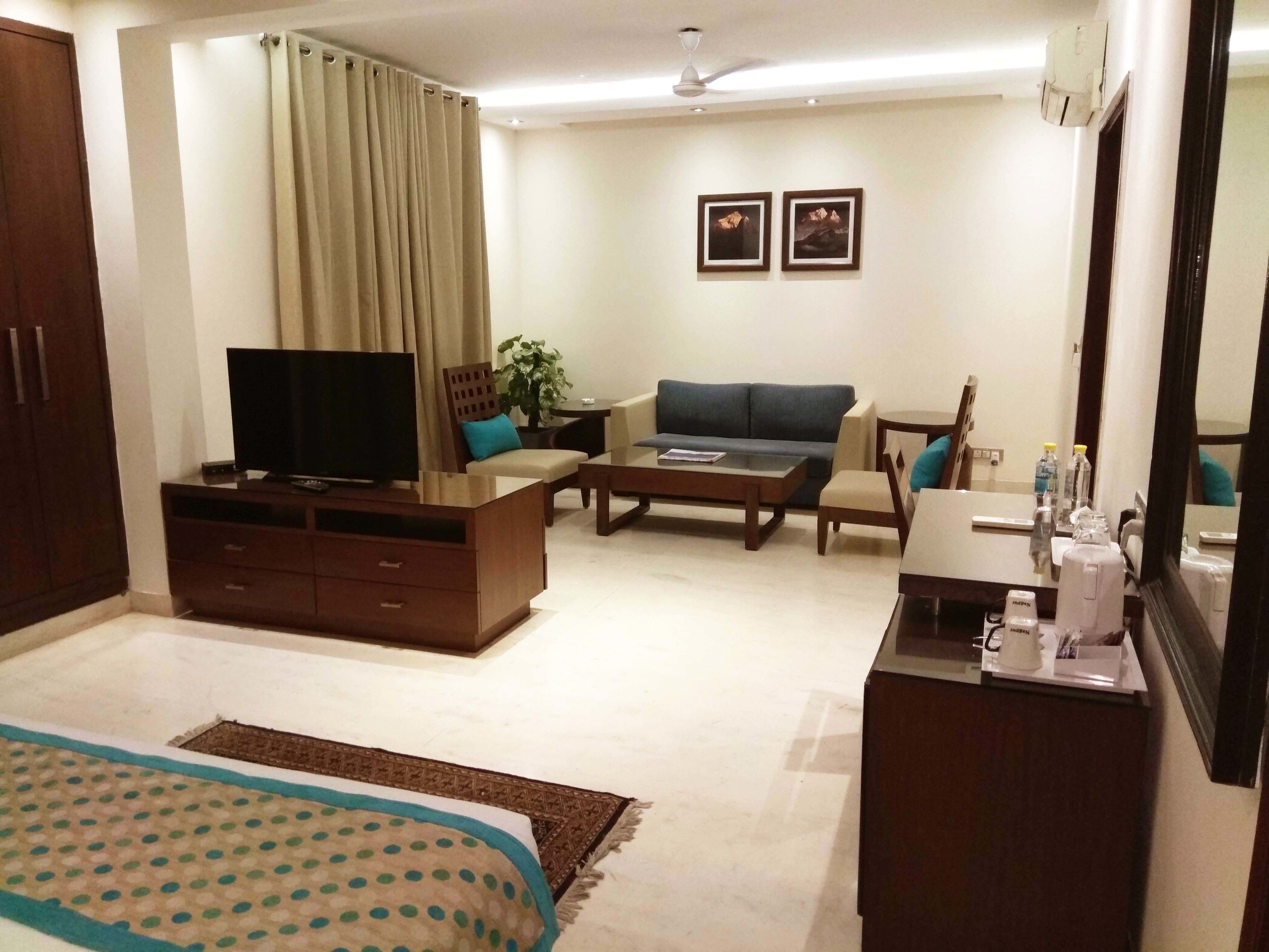 A hotel room with a bed, a TV, a sofa, a coffee table, a desk, and a mirror.