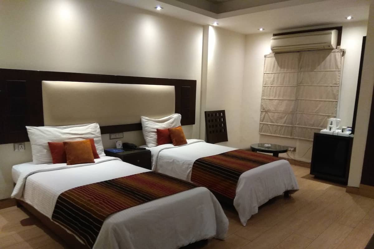 A hotel room with two beds, a bedside table with a lamp, a small round table, and a window with curtains.