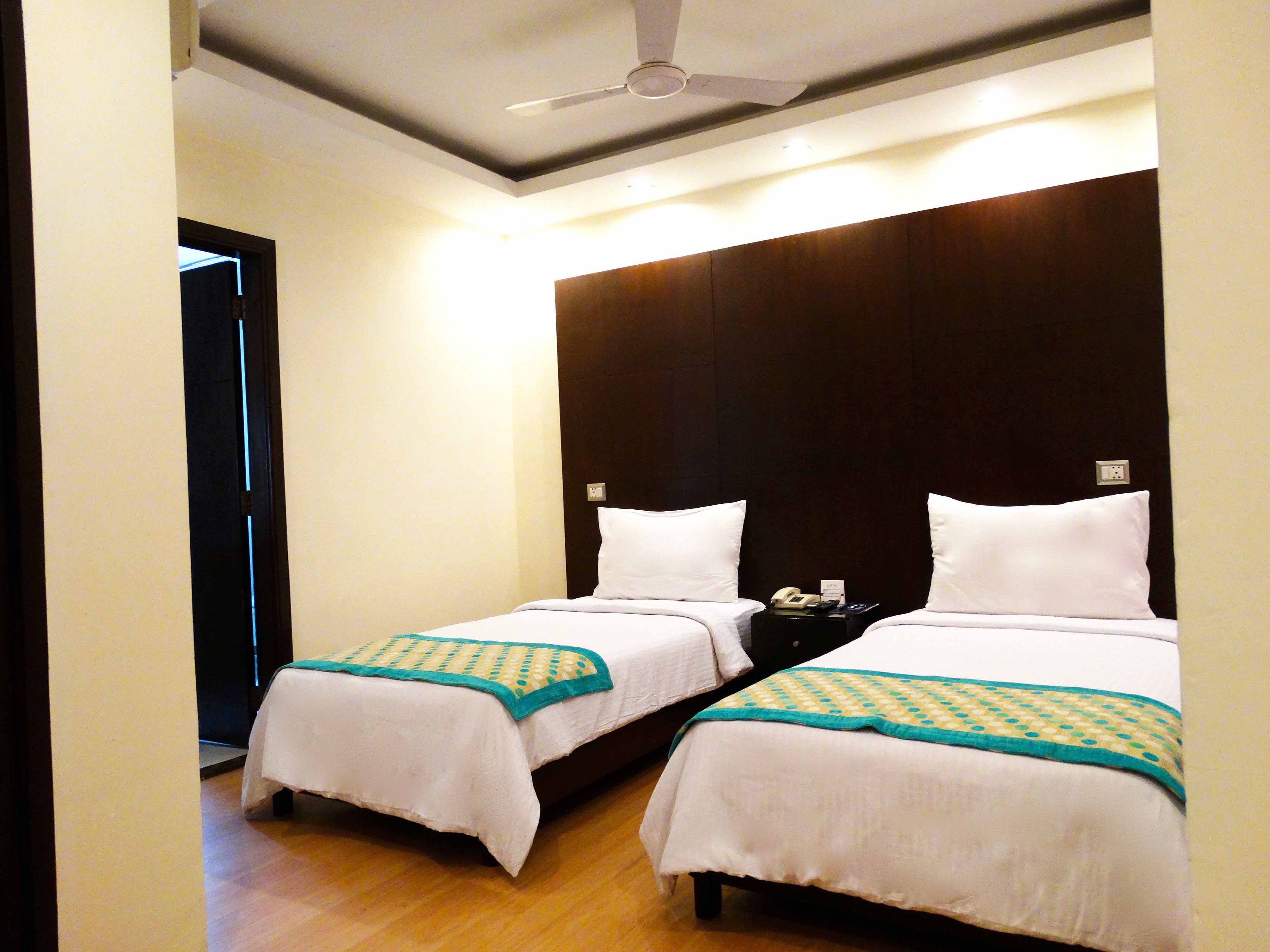 Une chambre d’hôtel avec deux lits simples, un ventilateur de plafond et une table de chevet avec un téléphone et une lampe.