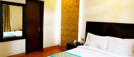 Habitación de hotel con cama, piso de madera, aire acondicionado instalado en la pared, una puerta y una mesita de noche con teléfono y lámpara.