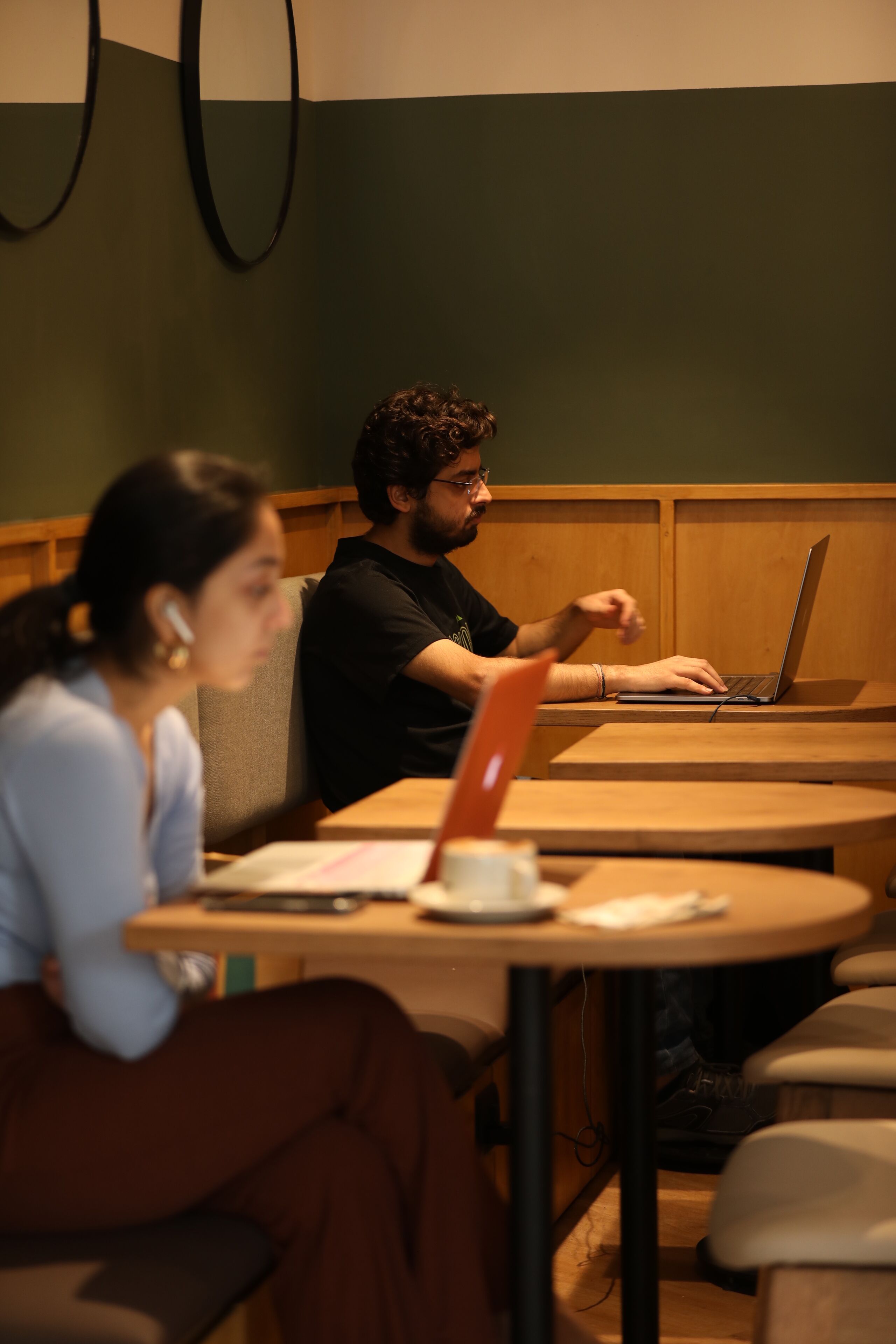 A person using a laptop at a wooden table in a room with green walls and wooden paneling.