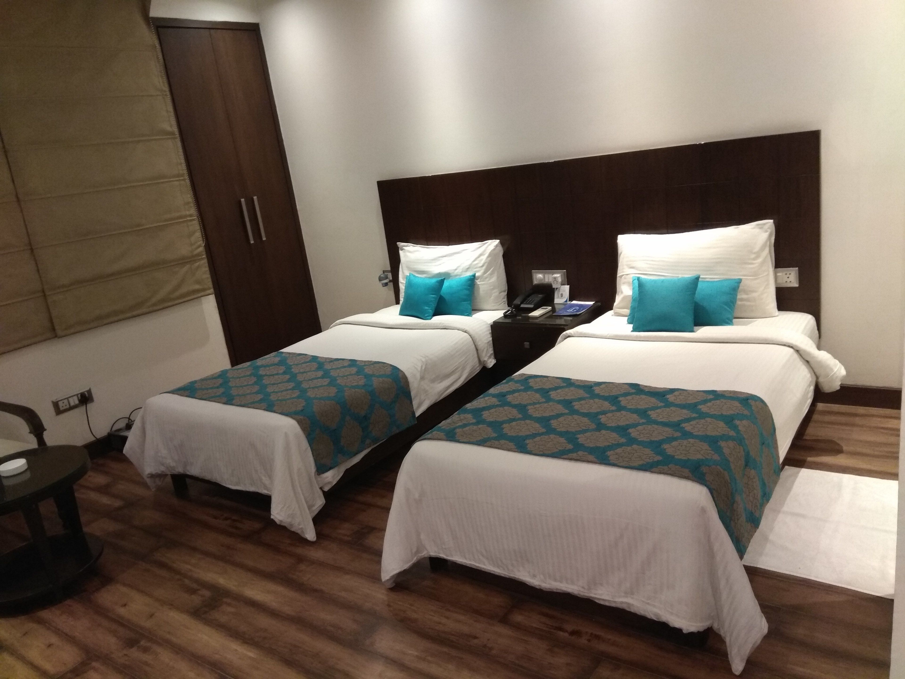 A hotel room with two single beds, a wooden floor, a wardrobe, and a desk with a telephone.