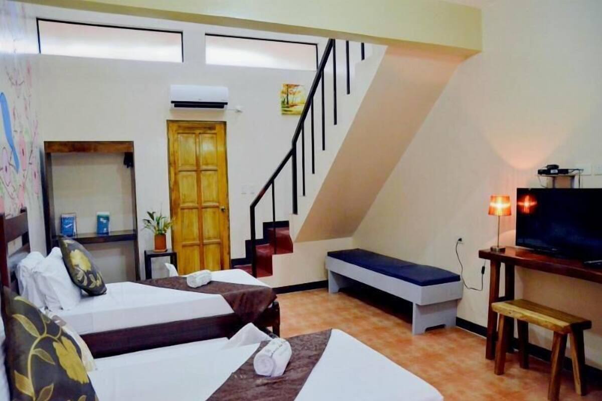 Een hotelkamer met twee bedden, een televisie, een bureau, een bankje, een trap en een deur.