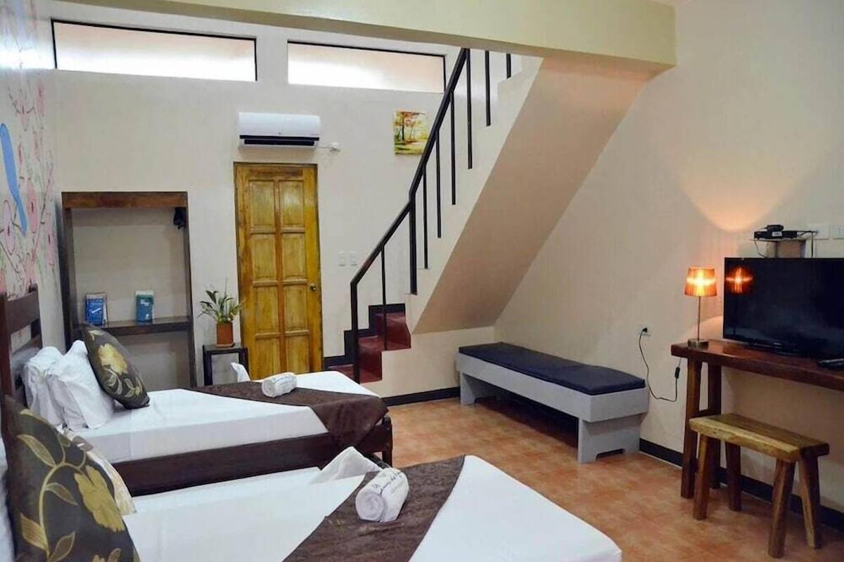 Een hotelkamer met twee bedden, een televisie, een bankje, een trap en een deur.