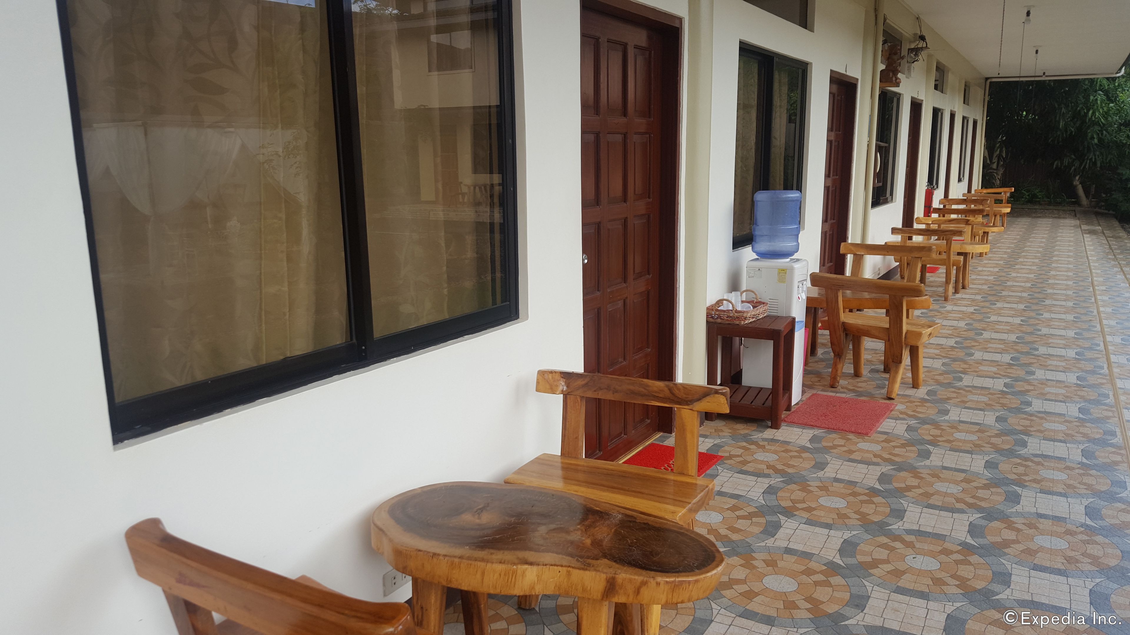 A corridor with wooden chairs and tables, a water dispenser, and a door.