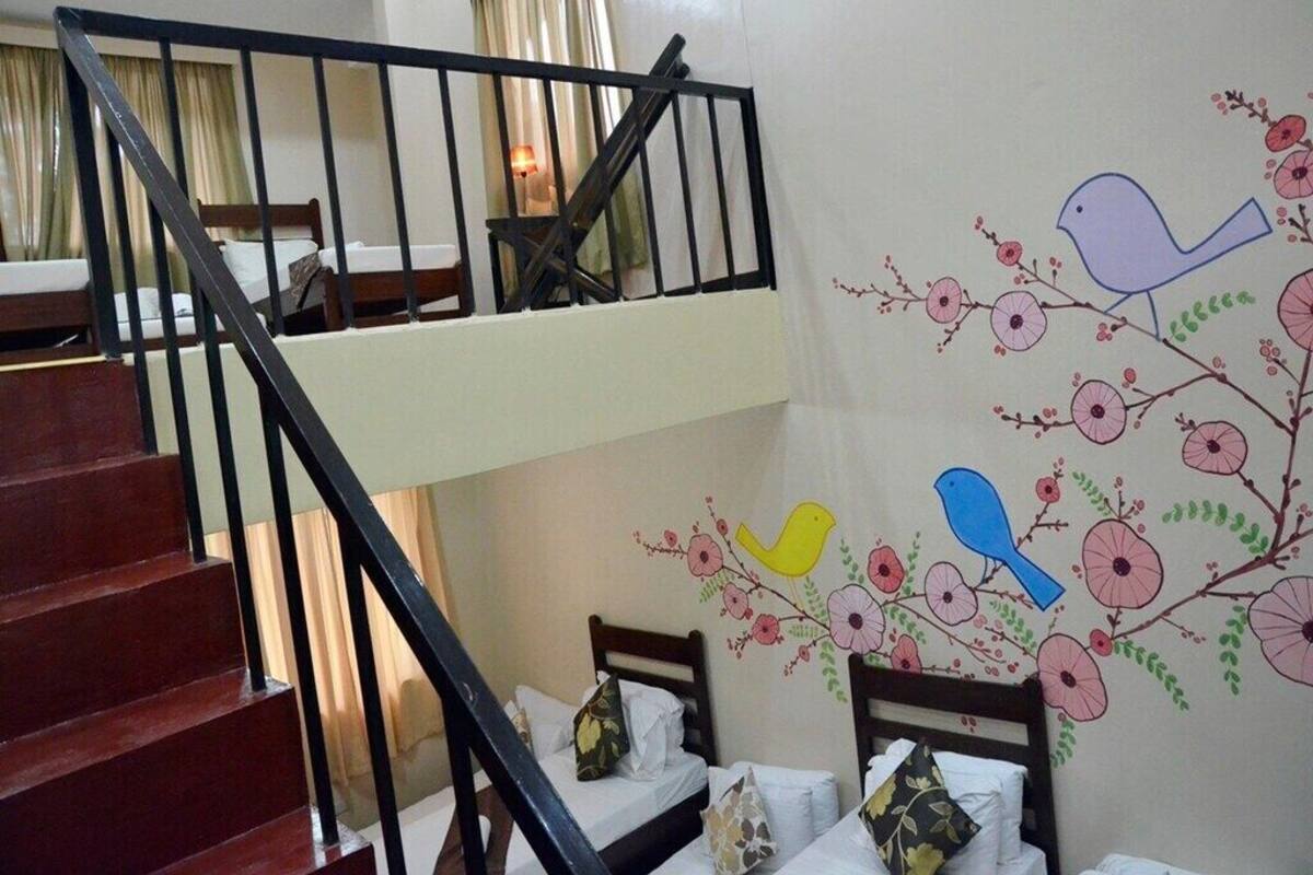 Een hotelkamer met een trap, twee bedden en een muurschildering van vogels en bloemen.