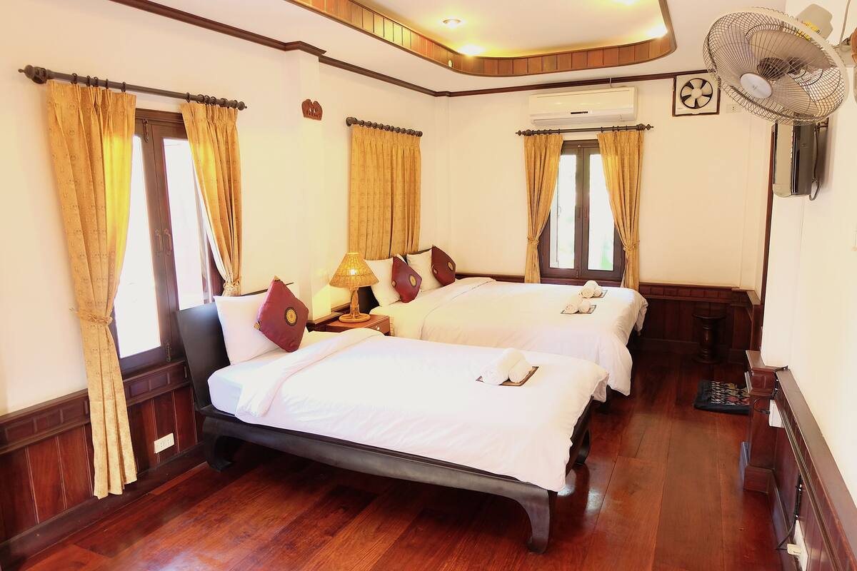 A hotel room with two beds, wooden flooring, and a ceiling fan.