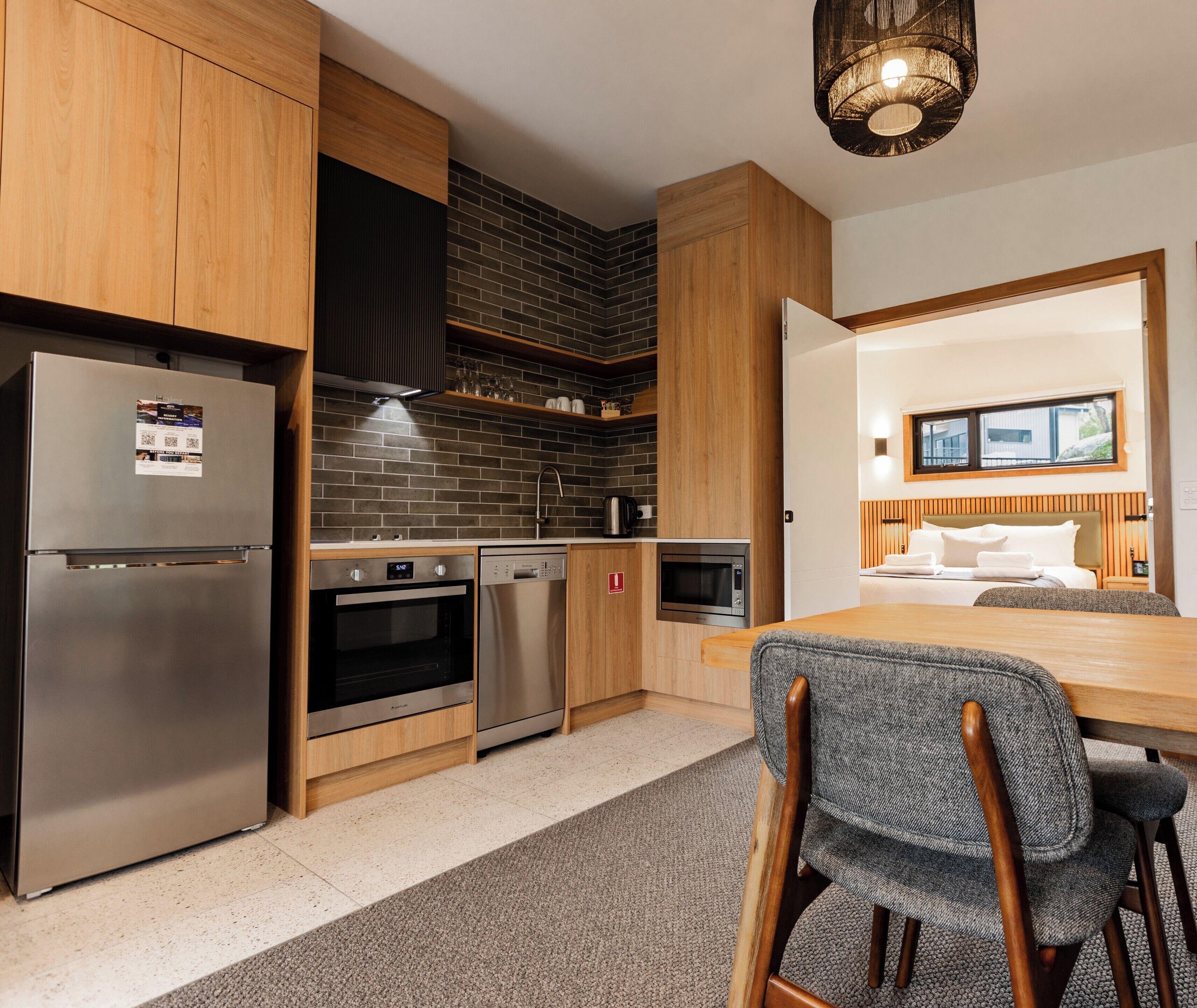 A modern kitchen with stainless steel appliances, a brick backsplash, and wooden cabinets.
