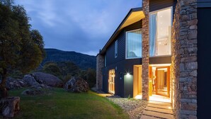 A modern house with a stone exterior, large windows, and a well-lit entrance. - Oaks Lake Crackenback Resort (Crackenback)