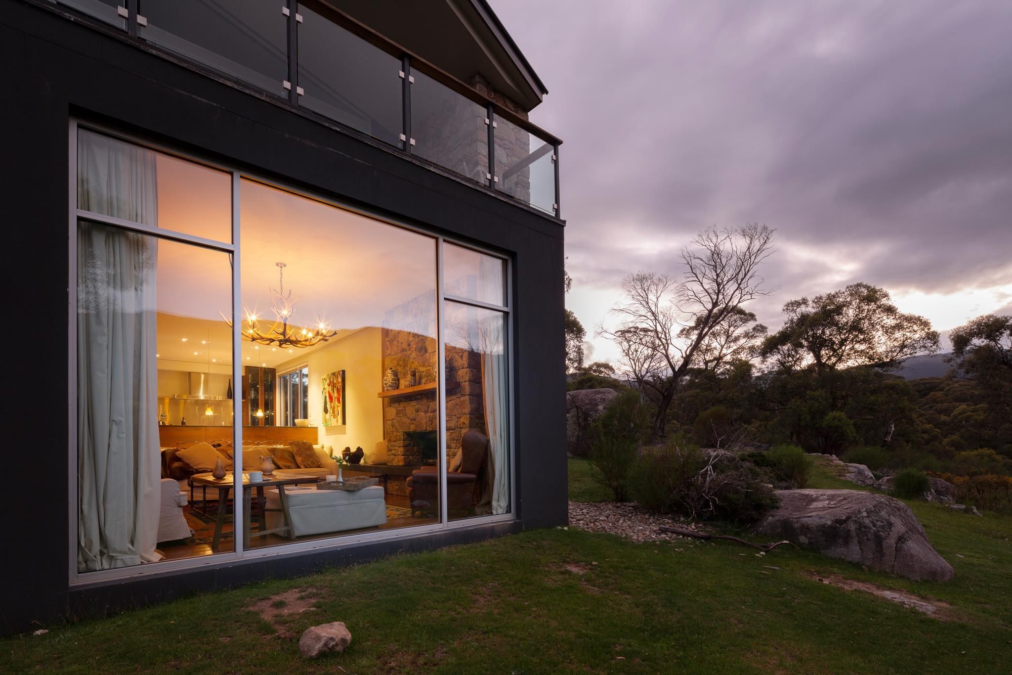 A modern house with large glass windows, a stone exterior, and a well-maintained lawn.
