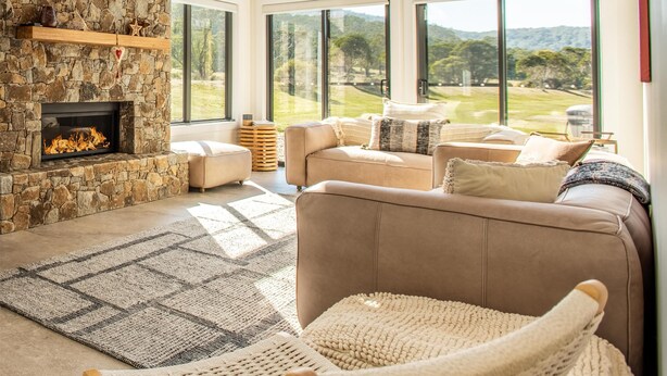 A cozy living room with a stone fireplace, large windows, and a view of the outdoors. - Oaks Lake Crackenback Resort (Crackenback)