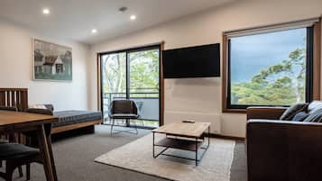 A modern living room with a wooden dining table, a sofa, and a TV mounted on the wall.