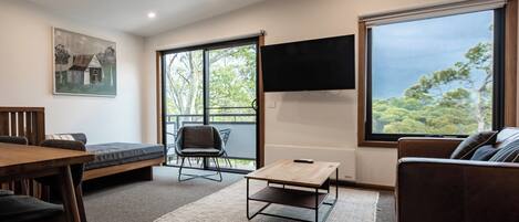 A modern living room with a wooden dining table, a sofa, and a TV mounted on the wall.
