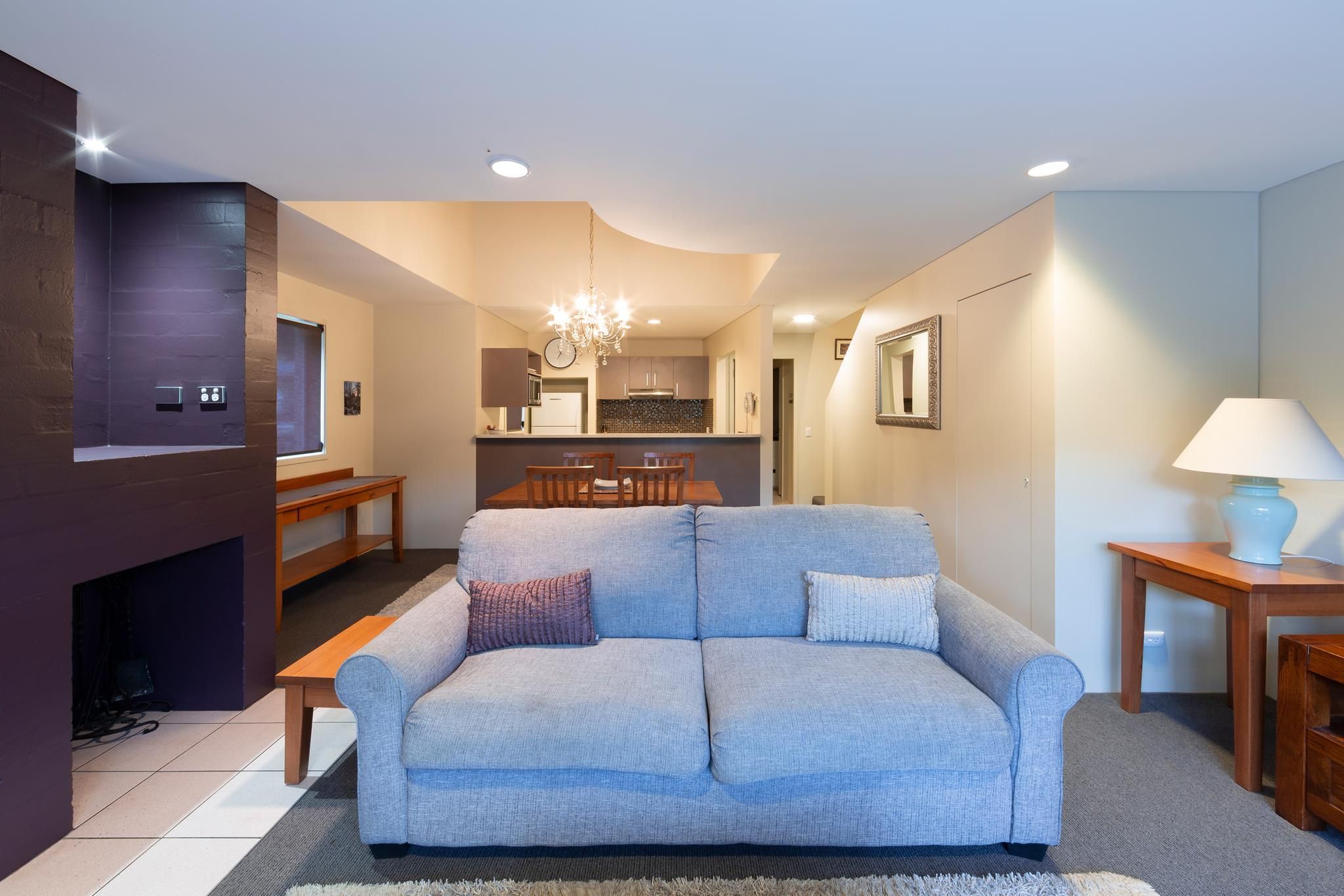 A modern living room with a sofa, a dining table, and a kitchen in the background.