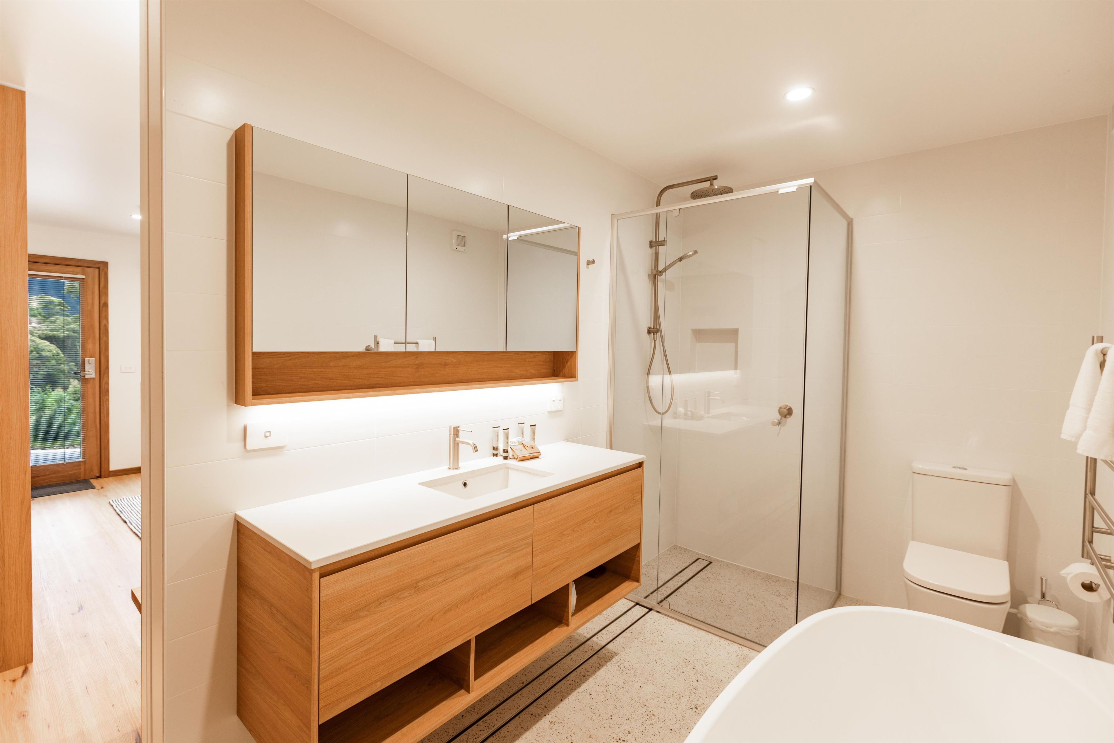 A modern bathroom with a large mirror, a wooden vanity, a shower enclosure, and a white bathtub.