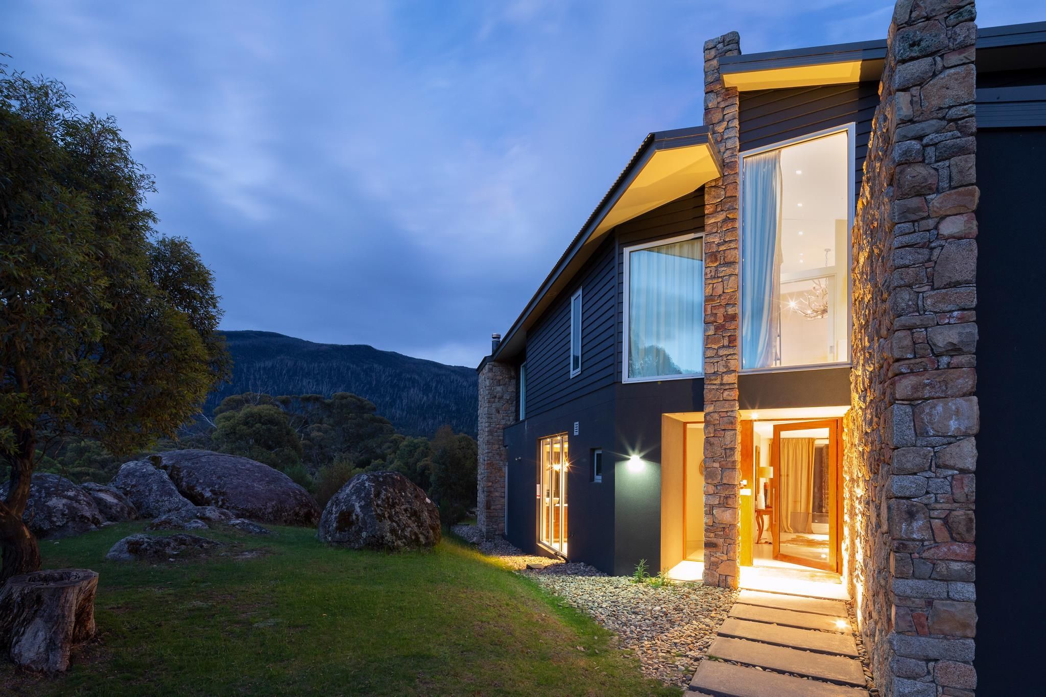 A modern house with a stone facade, large windows, and a well-lit entrance.