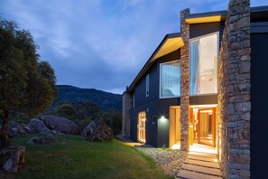 Une maison moderne avec une façade en pierre, de grandes fenêtres et une entrée bien éclairée.