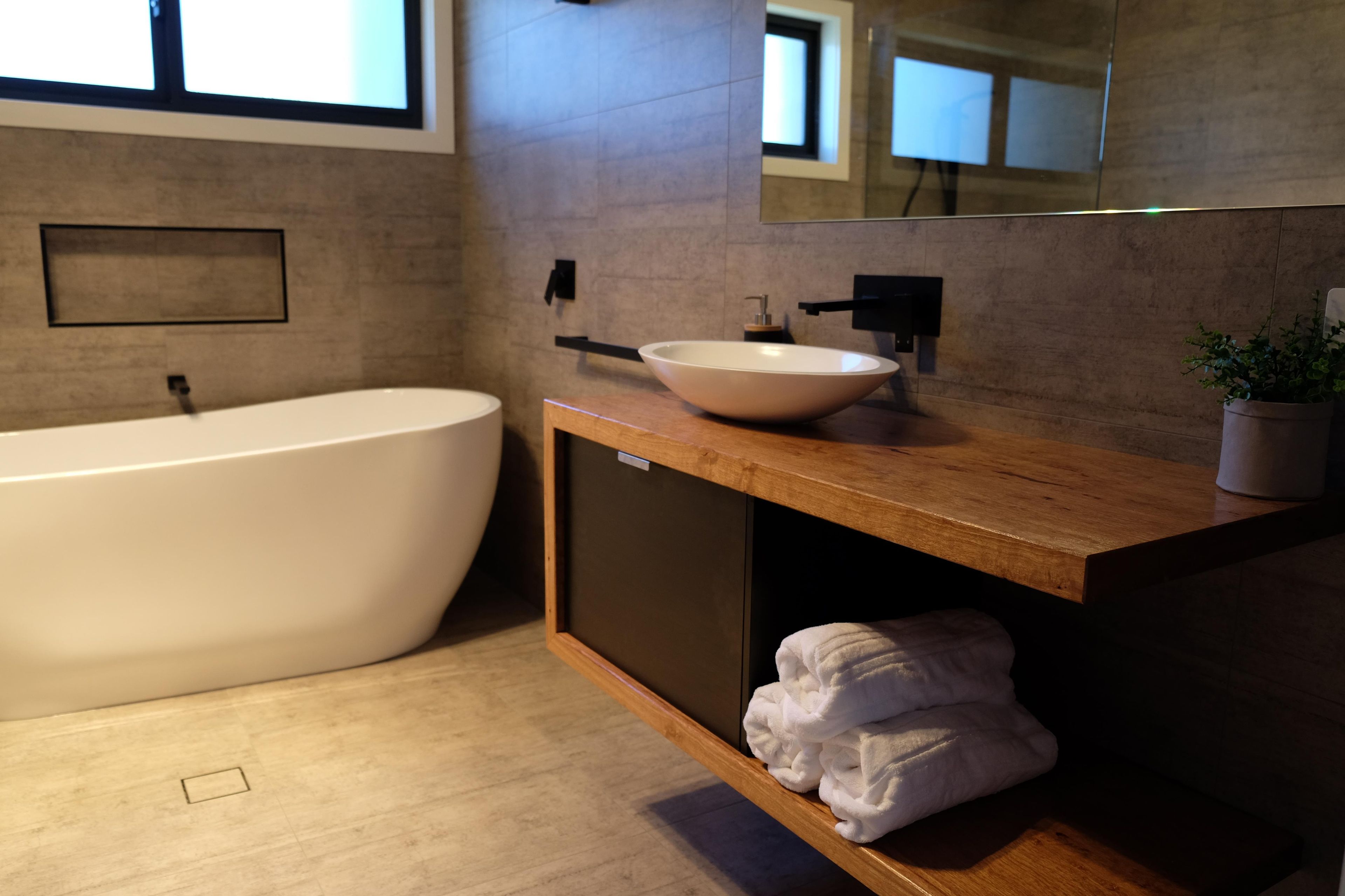 A modern bathroom with a freestanding bathtub, a vessel sink, and a wooden vanity with a towel rack.
