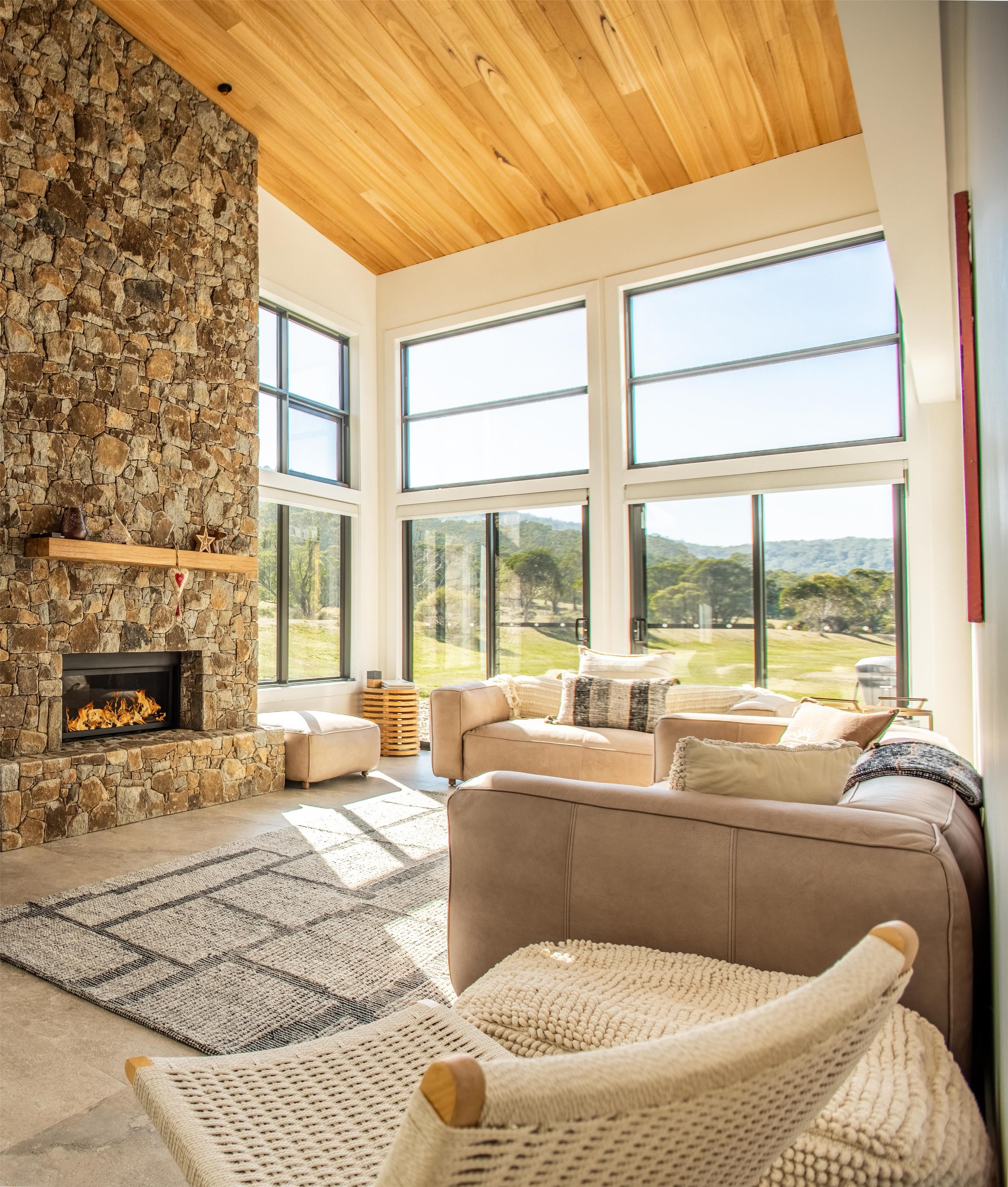 A spacious living room with a stone fireplace, large windows, and a view of a green landscape.
