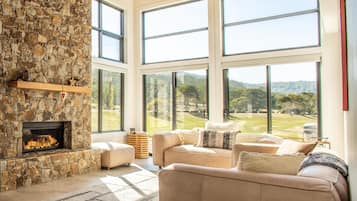 A spacious living room with a stone fireplace, large windows, and a view of a green landscape.