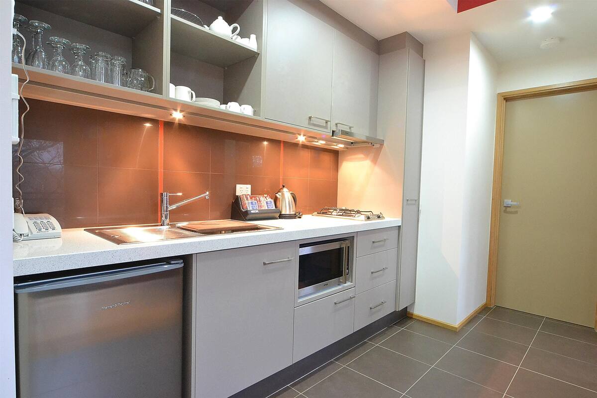 A modern kitchen with a dishwasher, oven, and a countertop with a kettle and coffee maker.