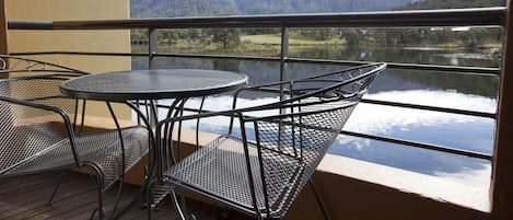 En balkon med et bord og stole, der giver udsigt over en sø og bjerge.