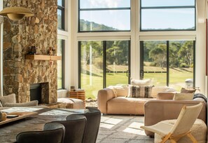Un vaste espace de vie agrémenté d’une cheminée en pierre, de sièges confortables et de grandes fenêtres offrant une vue sur un terrain de golf.