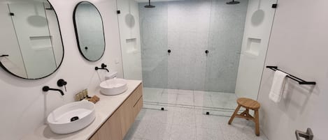Ett modernt badrum med två handfat, en stor spegel, en duschhörna och en träpall.