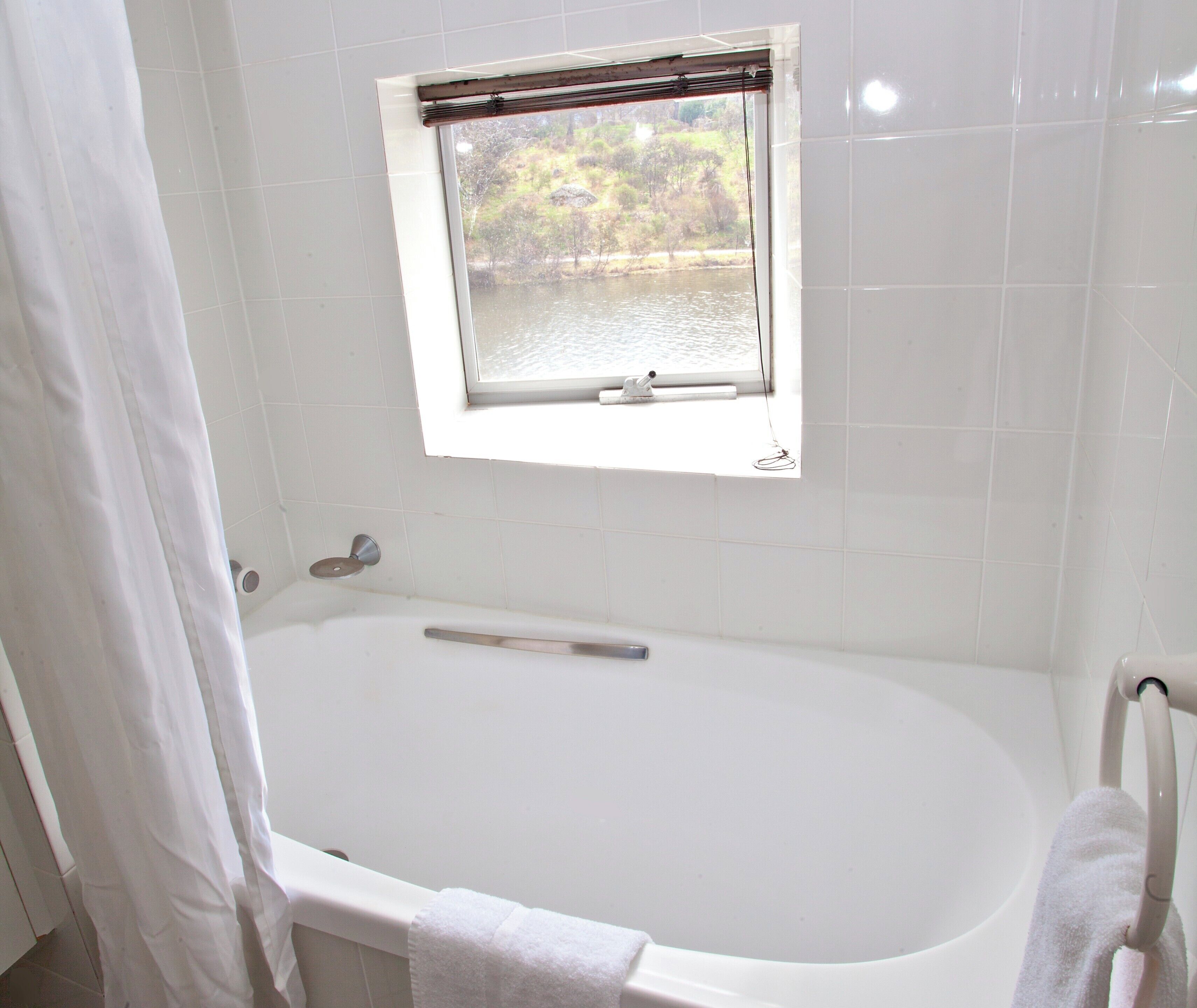 Une salle de bain avec une baignoire, une fenêtre donnant sur un plan d’eau et des arbres, et un porte-serviettes.