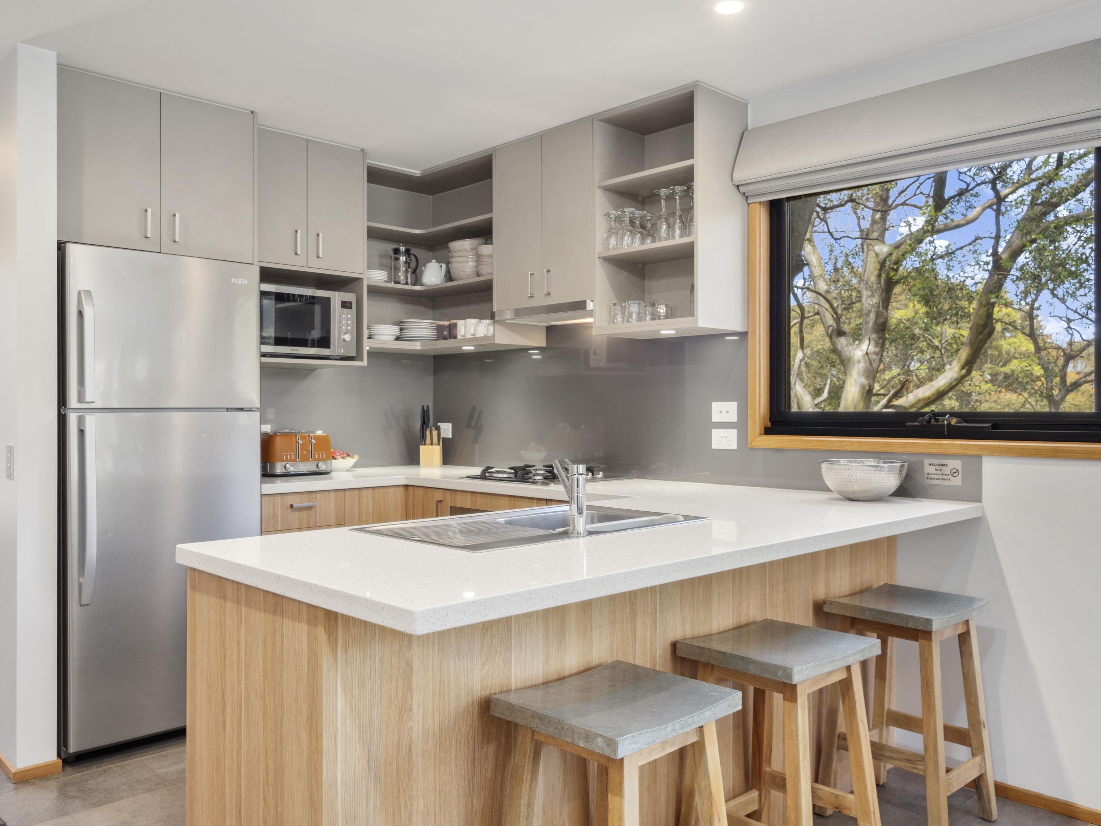 A modern kitchen with a central island, stainless steel appliances, and a window with a view of trees.