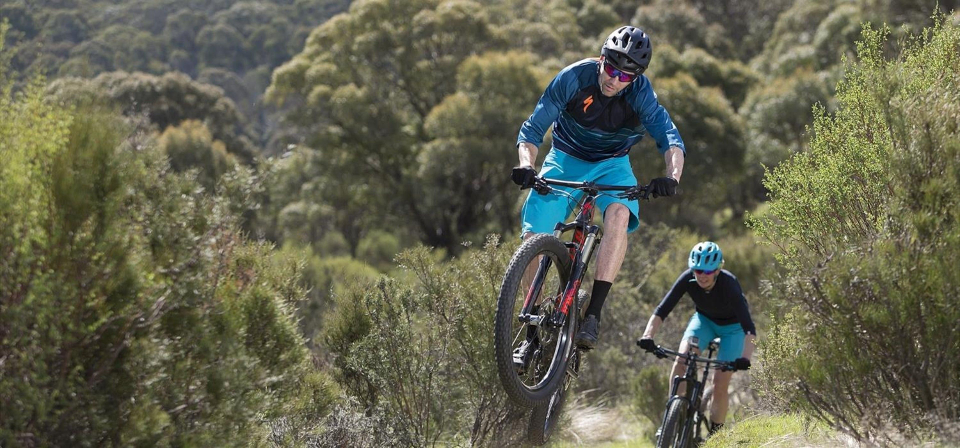 Two cyclists on a mountain bike trail surrounded by dense vegetation.