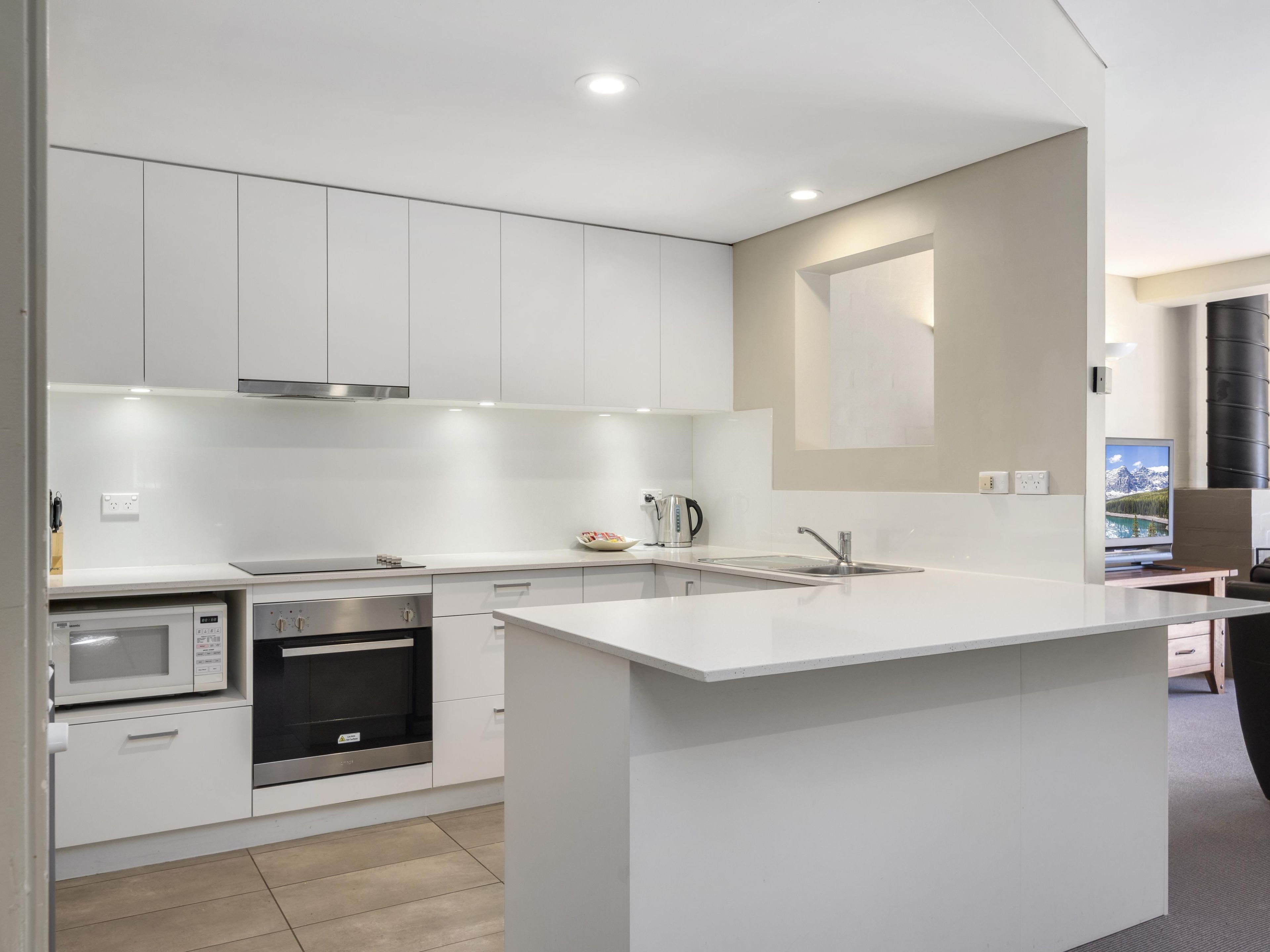 A modern kitchen with white cabinetry, a built-in oven, a microwave, and a large island with a sink.