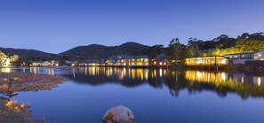 Un hotel sul lago, con acque calme che riflettono gli edifici, circondato da colline.