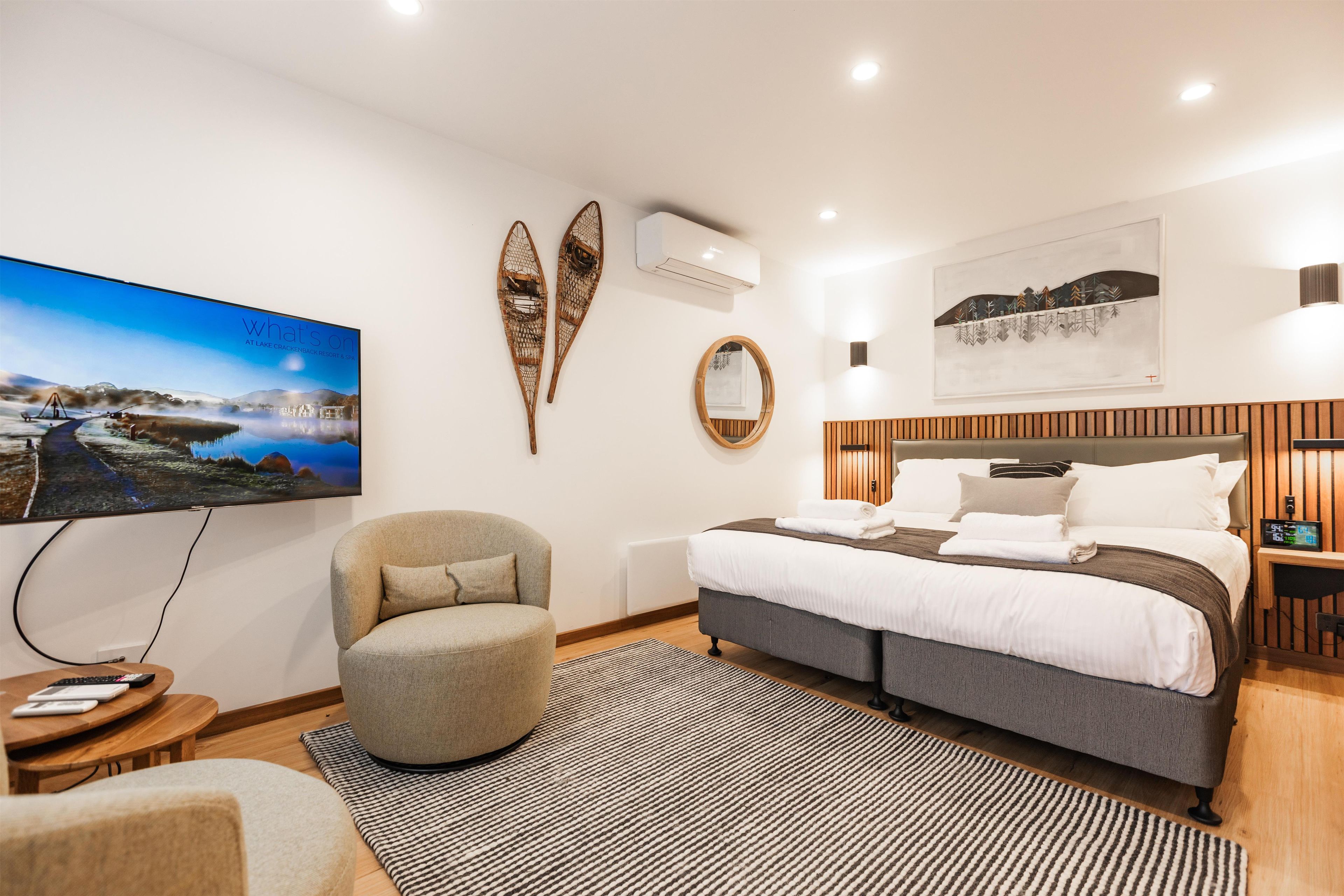 A modern hotel room with a bed, a chair, a television, and a wall-mounted air conditioner.