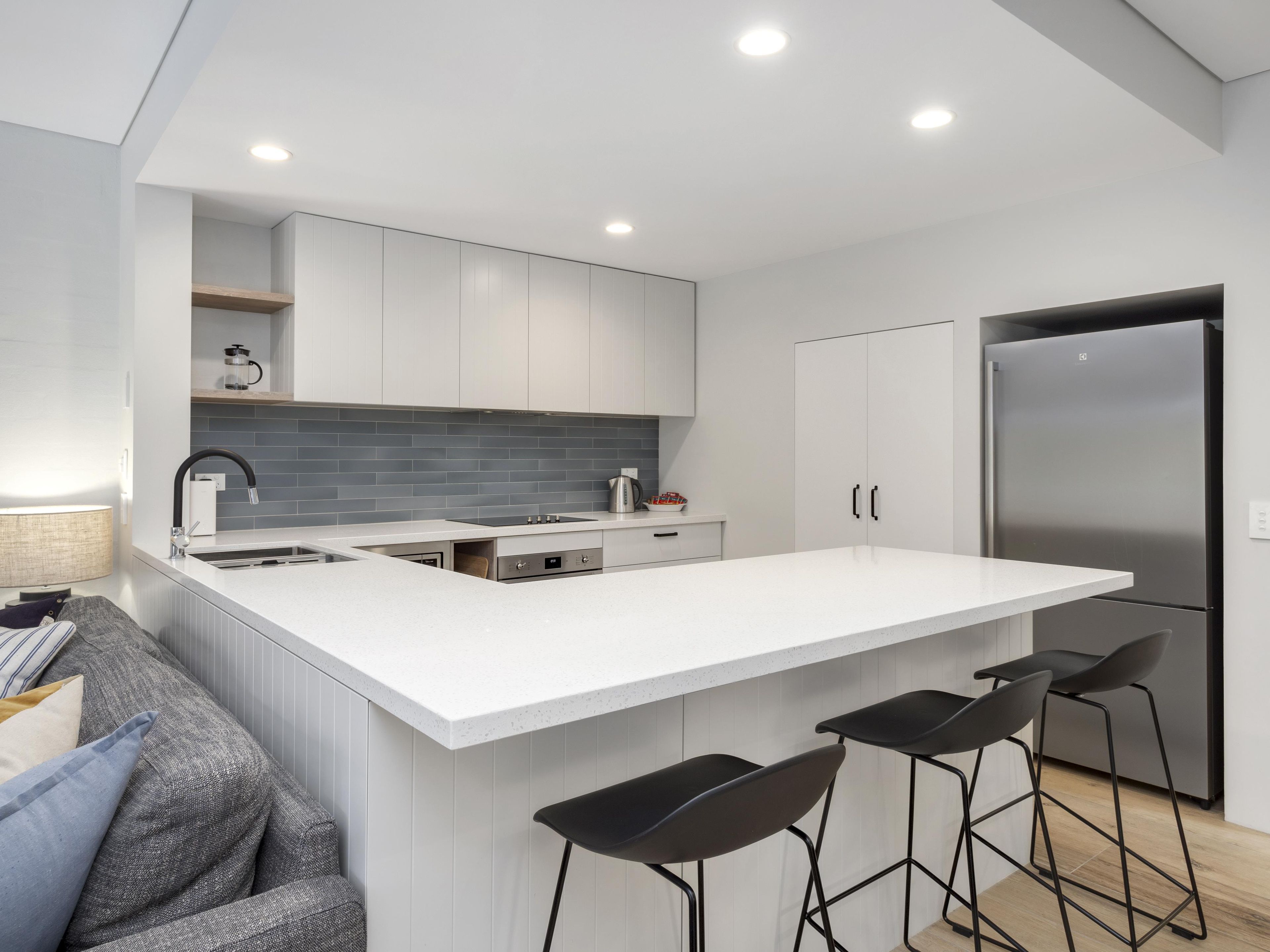 A modern kitchen with a large island, bar stools, and a built-in refrigerator.