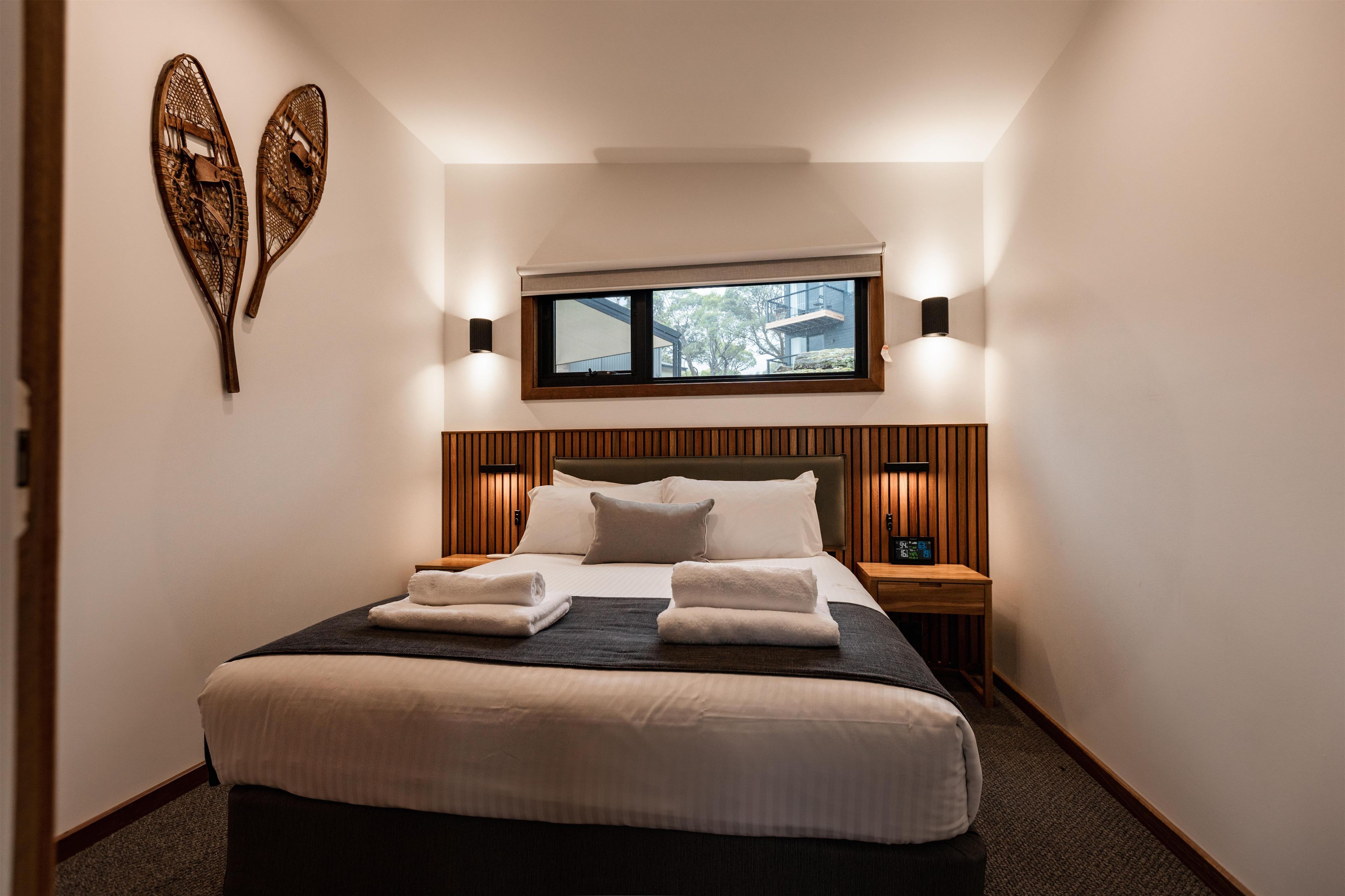 Una habitación de hotel con una cama grande, dos mesitas de noche, un ventanal y lámparas de pared.