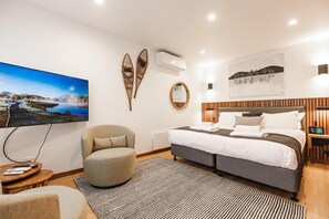 Una moderna camera d'hotel con un letto grande, una poltrona comoda, una TV a schermo piatto e un condizionatore d'aria a parete.