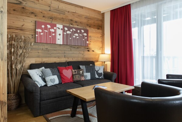 A living room with a wooden wall, a sofa, a coffee table, and a red curtain.