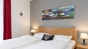 Et hotelværelse med en seng, to sengeborde, et natbord, en hjerteformet dekoration på væggen og et farverigt abstrakt billede.
