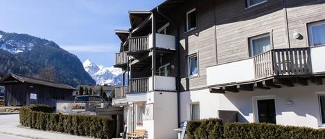 A multi-story building with balconies, a sign for Adler resort, and a mountain backdrop.