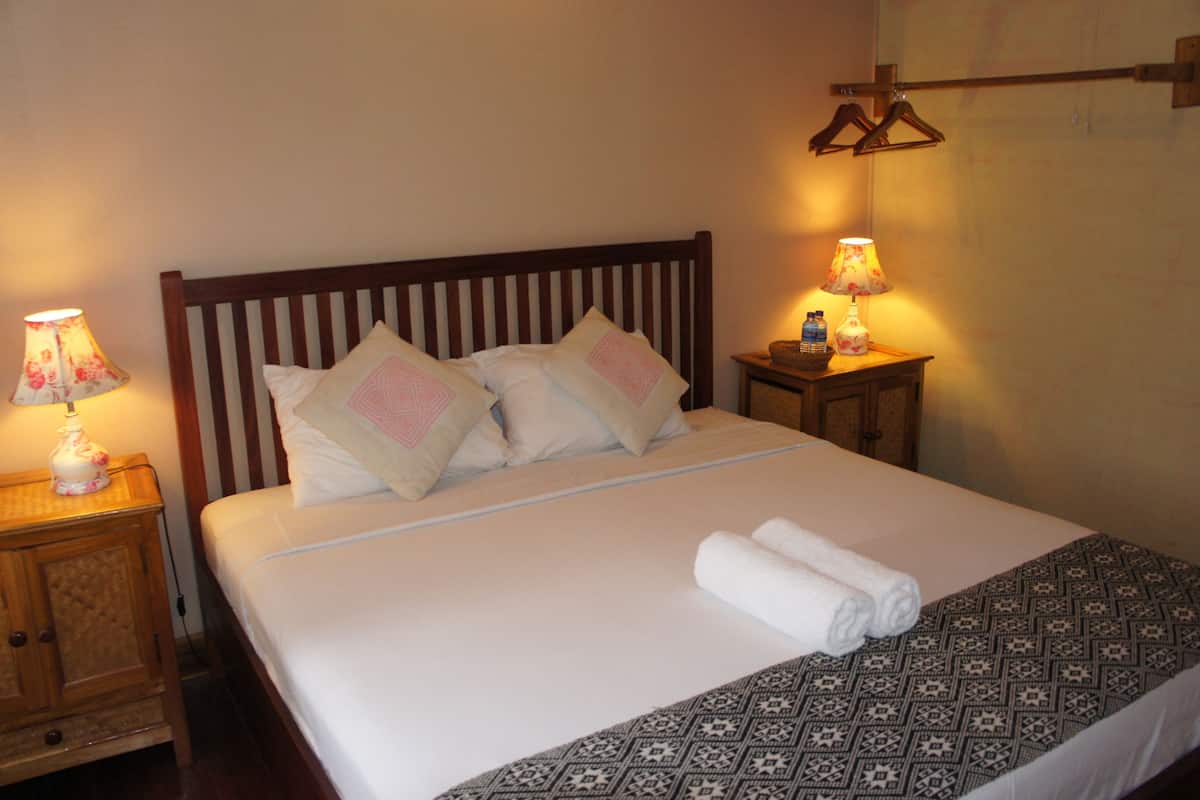 A neatly made bed with a patterned bedspread, two pillows, and a rolled towel. There are two bedside tables with lamps and a small basket on one.