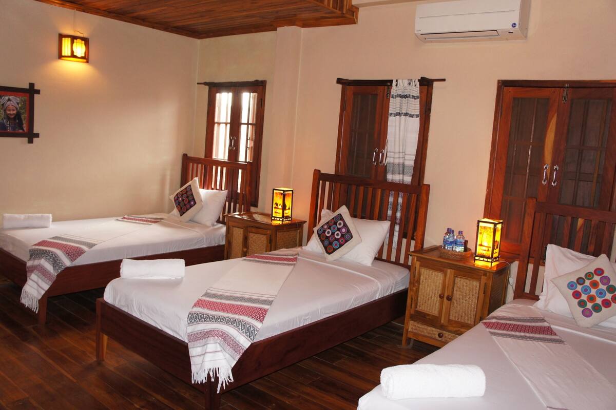 A hotel room with two single beds, wooden headboards, bedside tables with lamps, and a wooden wardrobe.