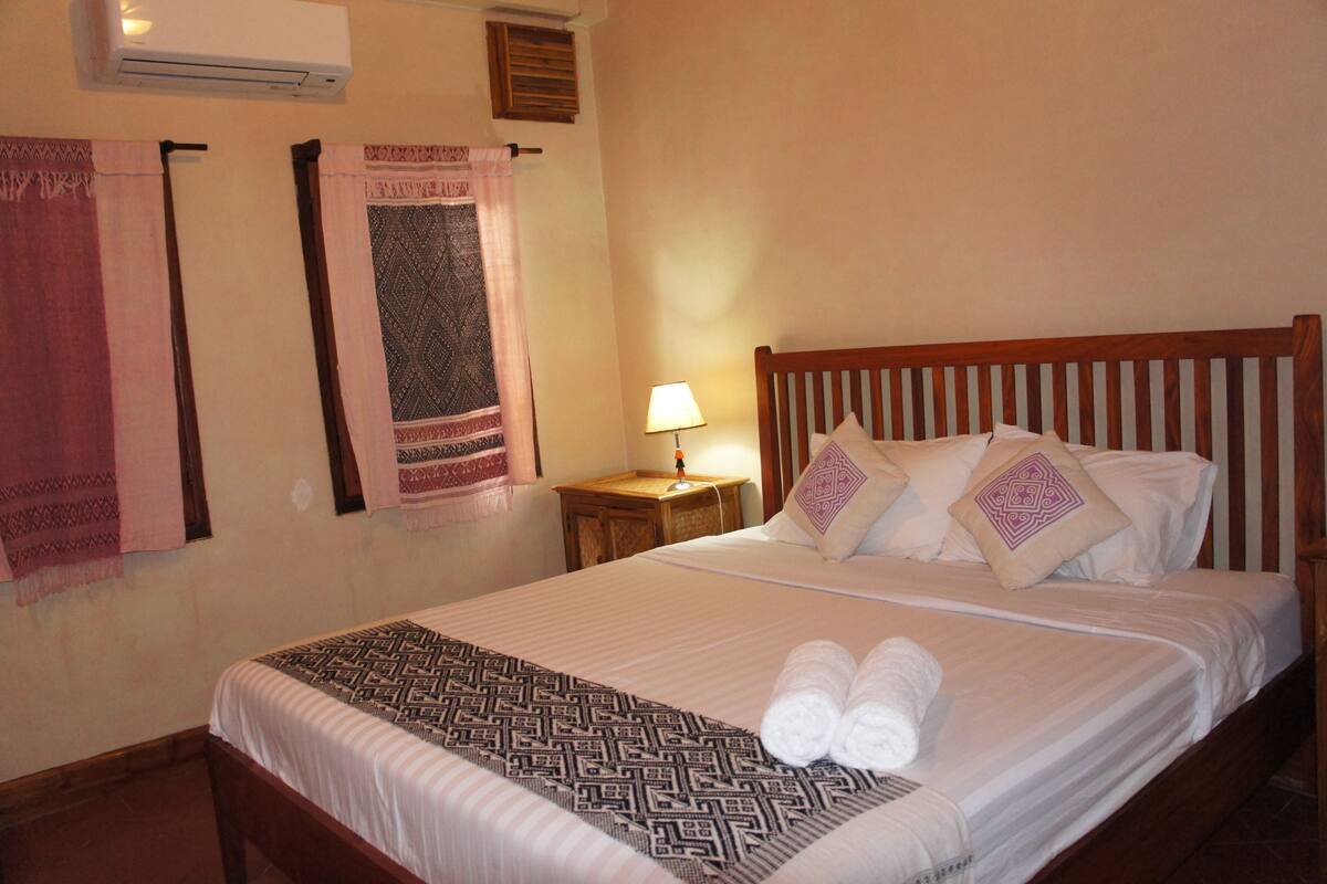 A neatly made bed with a patterned bedspread, pillows with geometric designs, and rolled towels on the bed.
